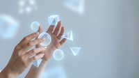 Hand touching holographic geometric shapes floating in air with glowing light effects on soft gray background for technology and innovation concepts.