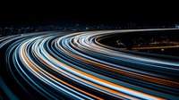 Curved light trails from vehicle headlights and taillights create glowing streaks against dark night sky, capturing urban traffic movement in long exposure photography.