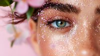 Young woman with bright blue eyes and glitter makeup in close up beauty portrait with pink floral elements and soft dreamy aesthetic.