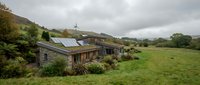 Modern eco-friendly house with solar panels nestled in green countryside landscape under cloudy sky, sustainable living concept for rural property development.