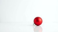 Red shiny Christmas ornament ball with metallic cap on white background, isolated for holiday design projects and seasonal decorations.