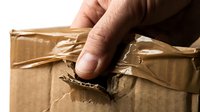 Unboxing damaged cardboard package with male hand tearing open torn kraft paper box for shipping and delivery concepts.
