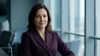 Professional businesswoman in purple suit smiling confidently in modern office with large windows. Corporate executive portrait for business presentations.
