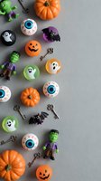 Halloween party decorations and spooky toys scattered on gray background with pumpkins, ghosts, bats, eyeballs and Frankenstein figures for seasonal celebration.
