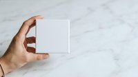Male hand holding blank white box on marble surface for product packaging mockup or branding presentation.