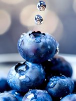Fresh blueberries with water drops falling in macro photography. Organic berries with morning dew showing natural texture and freshness against blurred background.