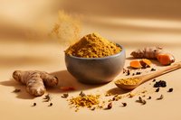 Aromatic turmeric powder in gray bowl with fresh ginger root, spices and wooden spoon on warm beige background with golden dust particles.
