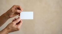 Close-up of mature male hands holding blank white business card against neutral beige background. Suitable for corporate branding, business identity, and professional marketing materials.