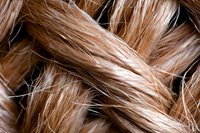 Close up macro shot of light brown natural hair strands showing texture and detail against dark background, highlighting shine and individual fibers.