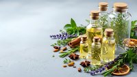 Natural essential oils in glass bottles with cork stoppers, fresh herbs, lavender, dried citrus and nuts for aromatherapy and wellness treatments.