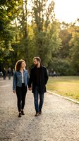 Happy interracial couple walking hand in hand through sunny park during golden hour sunset, enjoying romantic outdoor date together in natural setting.