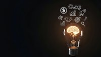 Glowing light bulb with brain inside surrounded by business icons on dark background representing innovation, creativity and entrepreneurship concepts.