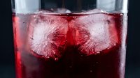 Chilled red berry drink with ice cubes in a glass, close-up shot on dark background for menu, bar, or beverage advertising.