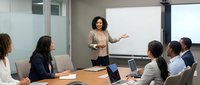 Professional African American businesswoman presenting to diverse team in modern conference room with whiteboard and laptops during corporate meeting.