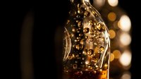 Golden liquid splashing in motion with bubbles and bokeh lights in background, suitable for beverage, alcohol, and luxury product advertising.