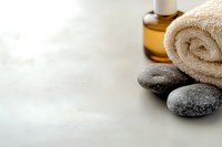 Spa wellness composition with massage stones, essential oil bottle and rolled white towel on light background. Wellness and relaxation concept.