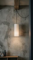 Cylindrical pendant light with frosted white glass shade suspended by black cord from wooden beam against weathered concrete wall, illuminating minimalist interior space with industrial aesthetic.