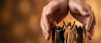 Protective hands covering diverse group of paper cutout people figures representing teamwork, unity, care, support, community protection and social responsibility.