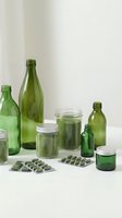 Green glass bottles jars and supplement capsules arranged on neutral background for eco-friendly packaging and natural health product design concepts.