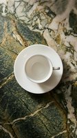 Empty white ceramic cup and saucer on marble surface with green and gold veining, overhead view. Suitable for café, restaurant, hospitality, and beverage marketing.