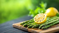 Fresh green asparagus spears and halved lemon on wooden cutting board against blurred garden background, natural food photography with soft lighting.