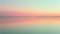 Serene sunset over calm water with soft pink and orange hues reflecting on glassy surface, ideal for peaceful backgrounds and nature-inspired designs.