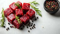 Raw beef cubes with rosemary sprigs and peppercorns on light background, fresh meat prepared for cooking, high protein food concept.