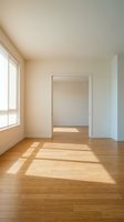 Empty room interior with natural sunlight streaming through window creating shadows on hardwood floor for real estate and home design projects.