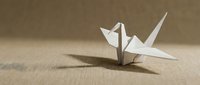 White origami crane on beige textured surface casting shadow in minimalist composition for meditation and zen concepts.