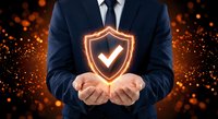 Businessman in suit holding glowing shield with checkmark symbol representing cybersecurity, data protection and business insurance concepts.