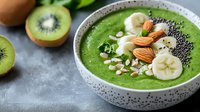 Green smoothie bowl with kiwi, banana slices, almonds, chia seeds and oats in ceramic bowl. Healthy breakfast superfood concept on gray background.