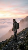 Male hiker with backpack standing on rocky mountain ridge overlooking sea of clouds at sunrise, adventure and outdoor exploration concept for travel and lifestyle use.