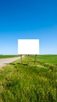 Blank white billboard sign on rural road with green grass field and clear blue sky for advertising and marketing campaigns.