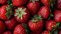 Fresh ripe strawberries with green leaves and stems in macro view showing natural texture and vibrant red color, suitable for food industry and healthy eating promotion.