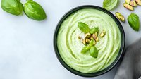 Creamy avocado pistachio dip garnished with fresh basil leaves and chopped nuts in black ceramic bowl on light background. Healthy vegan appetizer.