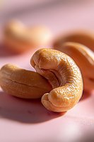 Fresh roasted cashew nuts macro shot on pink background showing detailed texture and natural curves of premium quality nuts for healthy snacking.
