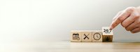 Hand placing wooden cube with 24/7 symbol next to blocks showing calendar, tools and clock icons representing continuous business service and support.