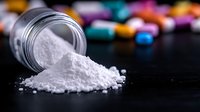 White powder spilling from glass container with colorful pharmaceutical pills scattered in background on dark surface, medical and healthcare concept.