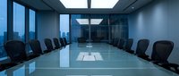 Modern corporate boardroom with glass conference table and executive chairs overlooking city skyline through floor-to-ceiling windows for business meetings.