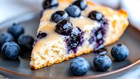 Fresh blueberry cheesecake slice on dark plate with whole berries, showing creamy texture and juicy fruit. Close up macro food photography reveals rich details.