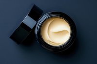 Luxury face cream in open black jar on dark background, top view. Premium skincare moisturizer with golden texture for beauty and cosmetic concepts.
