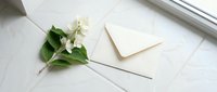 White jasmine flowers with green leaves and closed envelope on marble surface, suitable for wedding invitations, stationery design, and greeting card layouts.