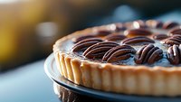 Chocolate ganache tart with swirled dark chocolate topping on shortcrust pastry base, close-up view showing glossy texture and decorative pattern.