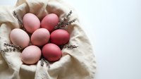 Pink and coral colored Easter eggs arranged in linen cloth with dried lavender sprigs for spring holiday celebration and seasonal decoration.