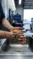 Mechanic washing dirty hands with soap at garage sink after automotive repair work. Professional hygiene and cleanliness in workshop environment.