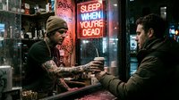 Tattooed male bartender with facial hair serving drink to customer at neon-lit bar counter at night, urban nightlife scene.