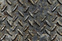 Weathered industrial diamond plate steel surface with raised anti-slip pattern showing wear, rust and metallic texture in dark gray tones.
