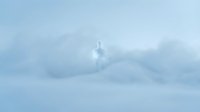 Silhouette of a person standing alone on snowy mountain peak surrounded by thick clouds and fog, conveying isolation, solitude, and contemplation in winter landscape.