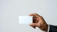 Dark-skinned male hand in business attire holding blank white card against neutral background for corporate branding and professional mockup purposes.