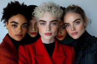 Diverse group of young female models with different skin tones and features wearing red and dark coats pose together in modern beauty portrait with natural makeup.